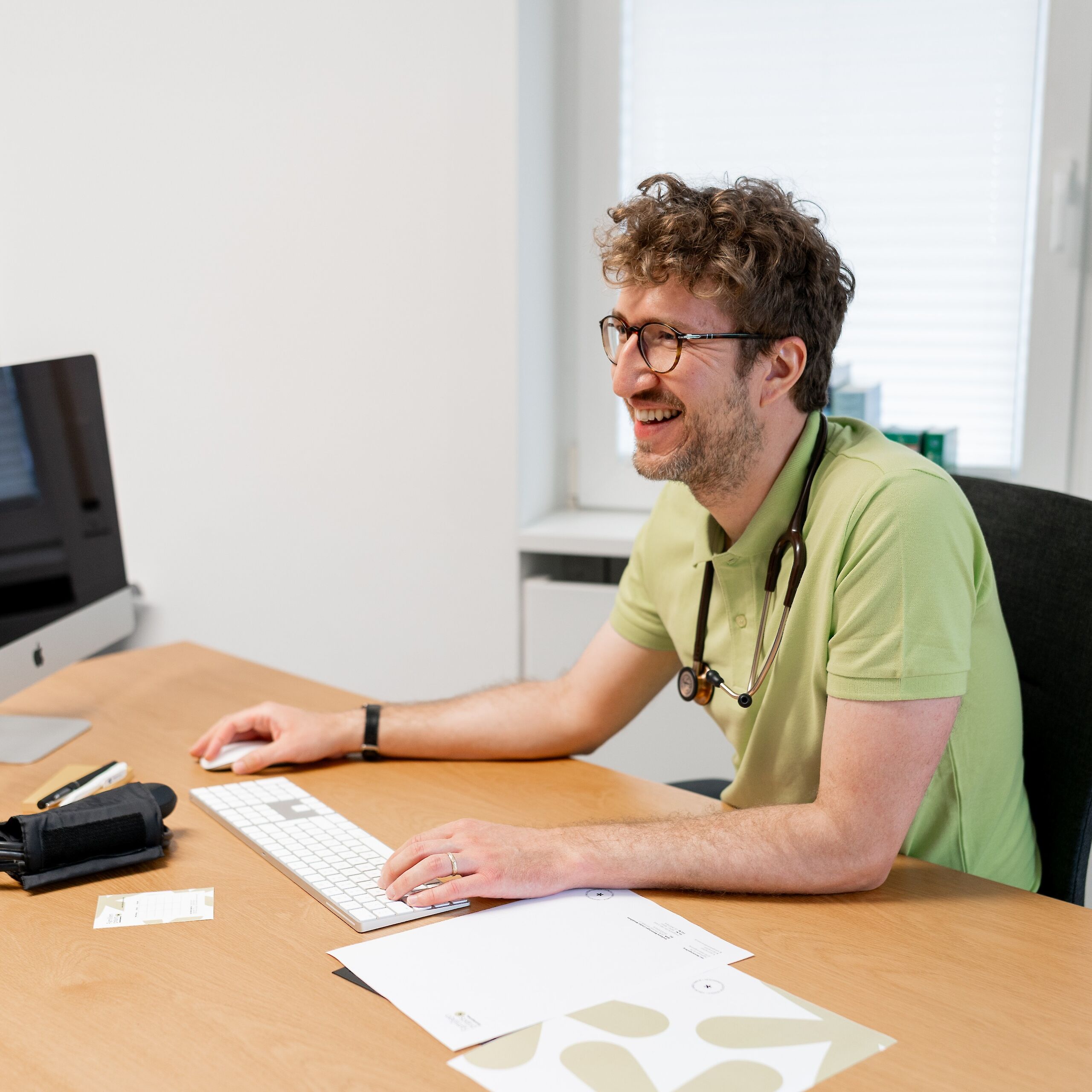 Arzt sitzt am Schreibtisch mit Computer und Briefpapier