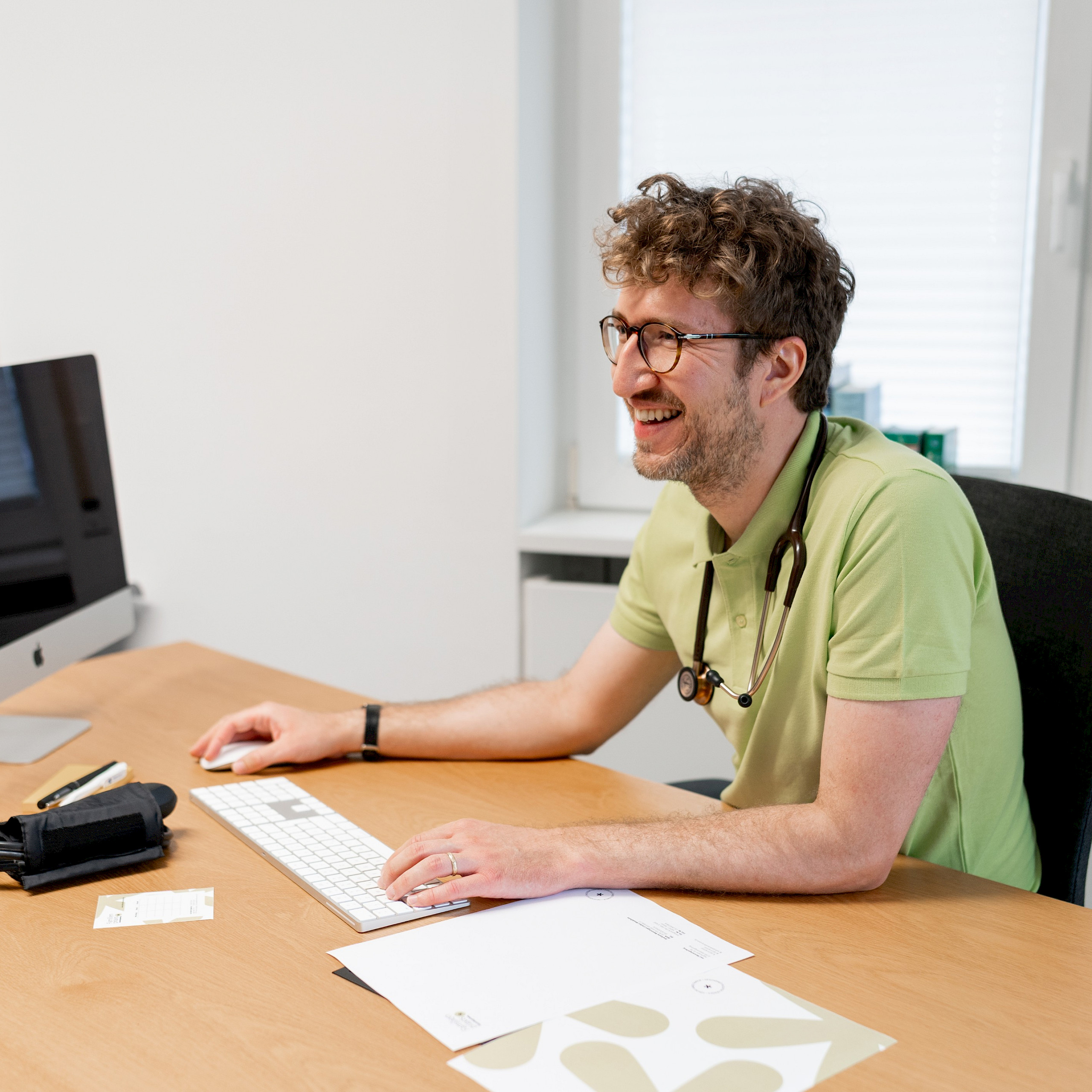 Arzt sitzt am Schreibtisch mit Computer und Briefpapier